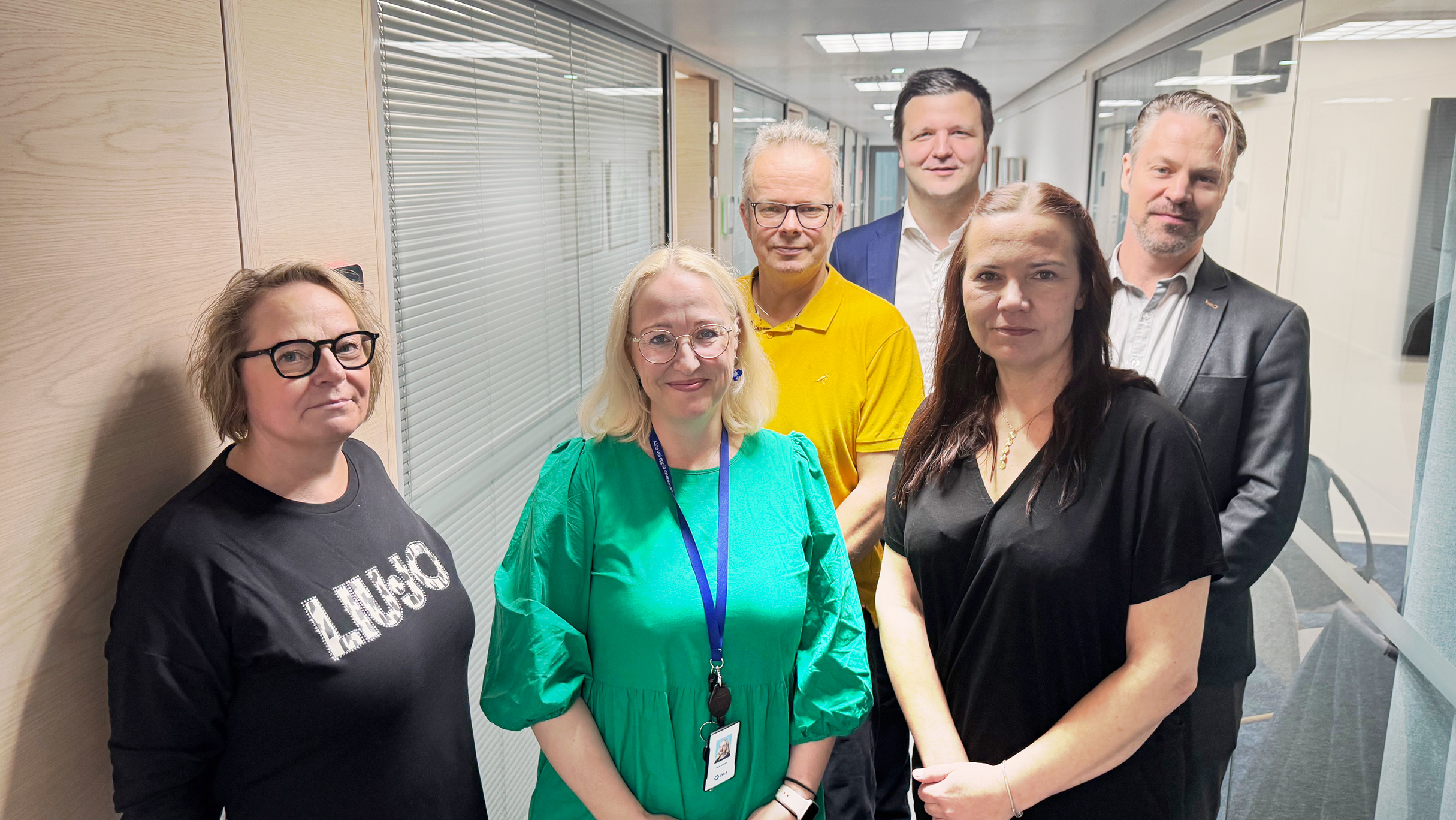 Neljä naista ja kaksi miestä seisoo Akavatalon käytävällä katsoen kameraan