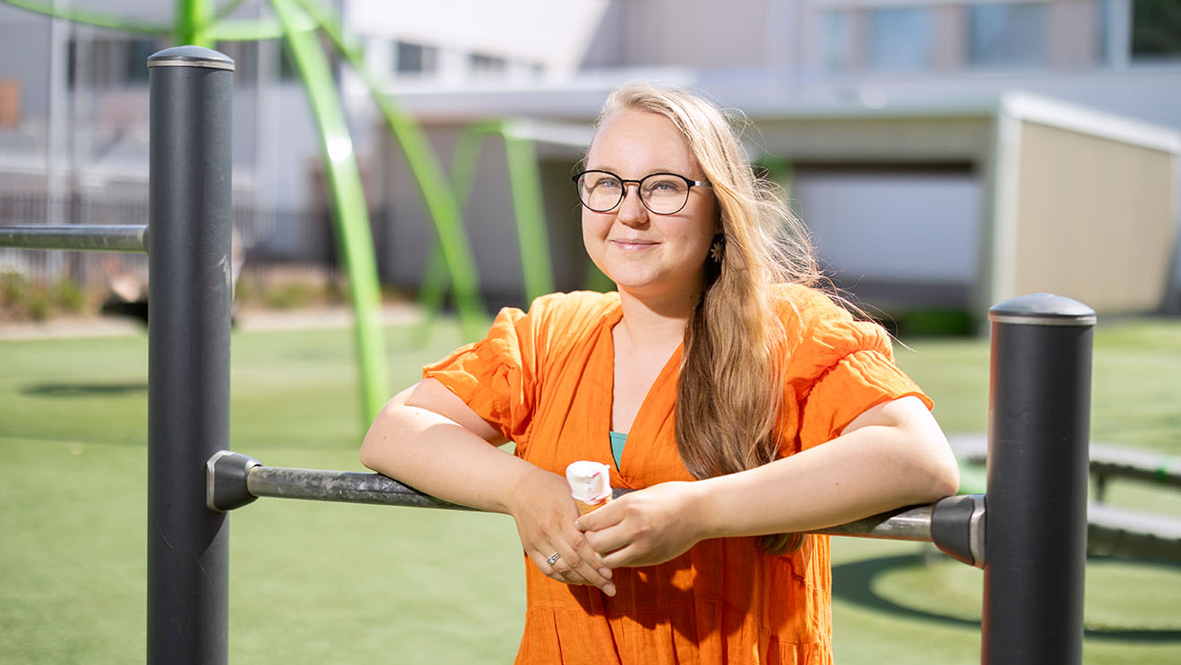 Henkilö nojaa jäätelö kädessään leikkitelineeseen koulun pihalla. 